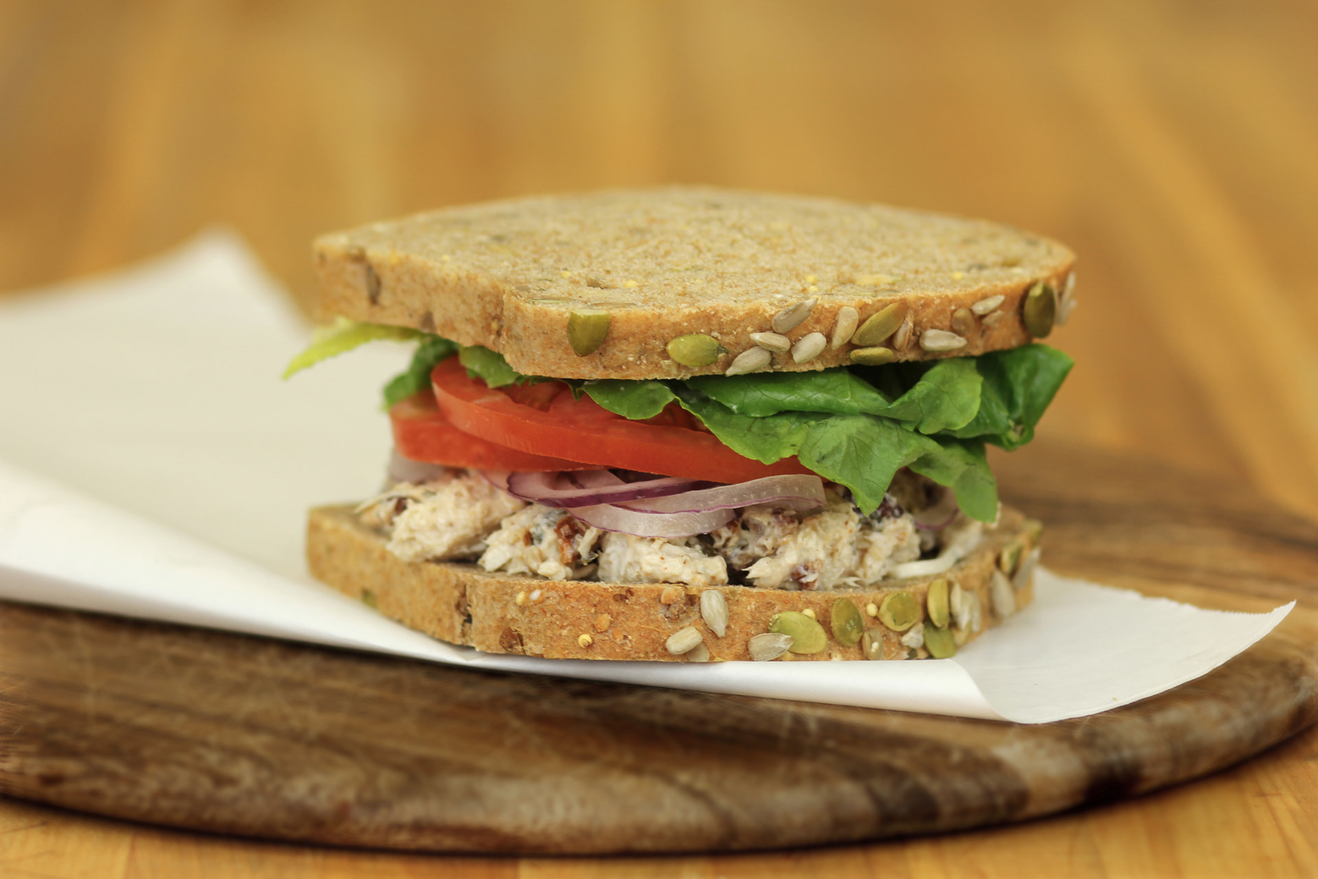 Louisville chicken salad sandwich on seeded whole grain bread with lettuce, tomato and red onion