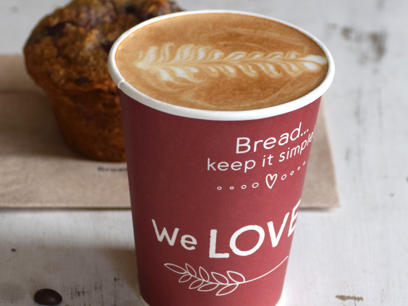 Latte with leaf latte art in a Great Harvest cup beside a muffin
