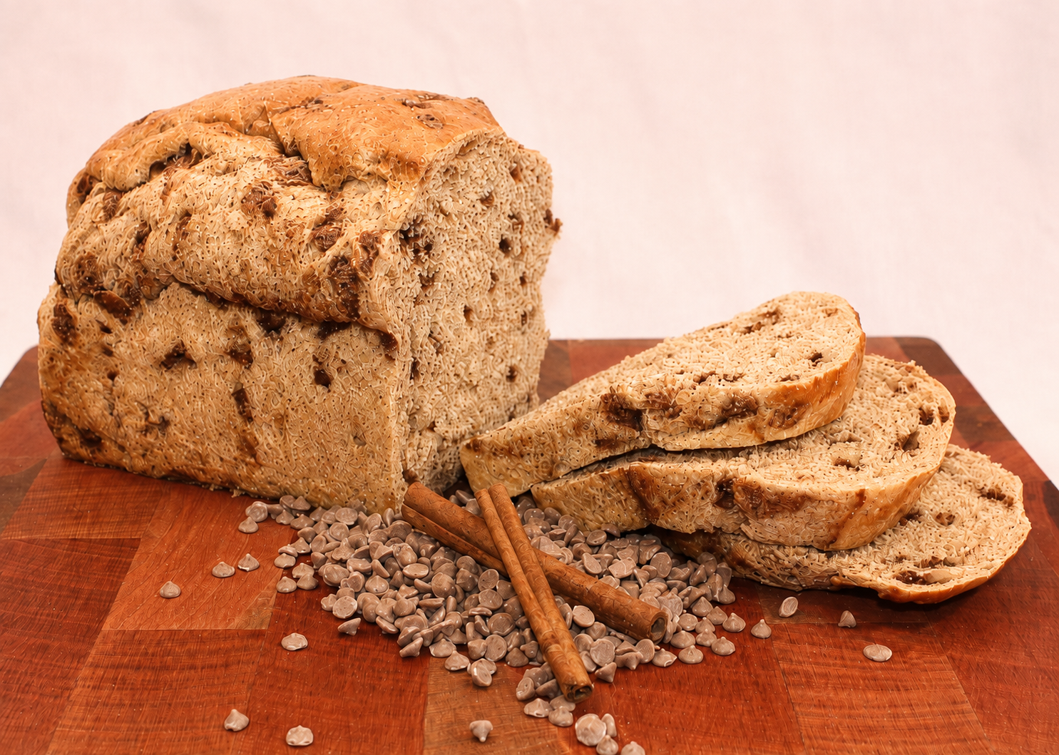 Whole Wheat Cinnamon Chip loaf sliced on a wooden board with cinnamon chips and cinnamon sticks