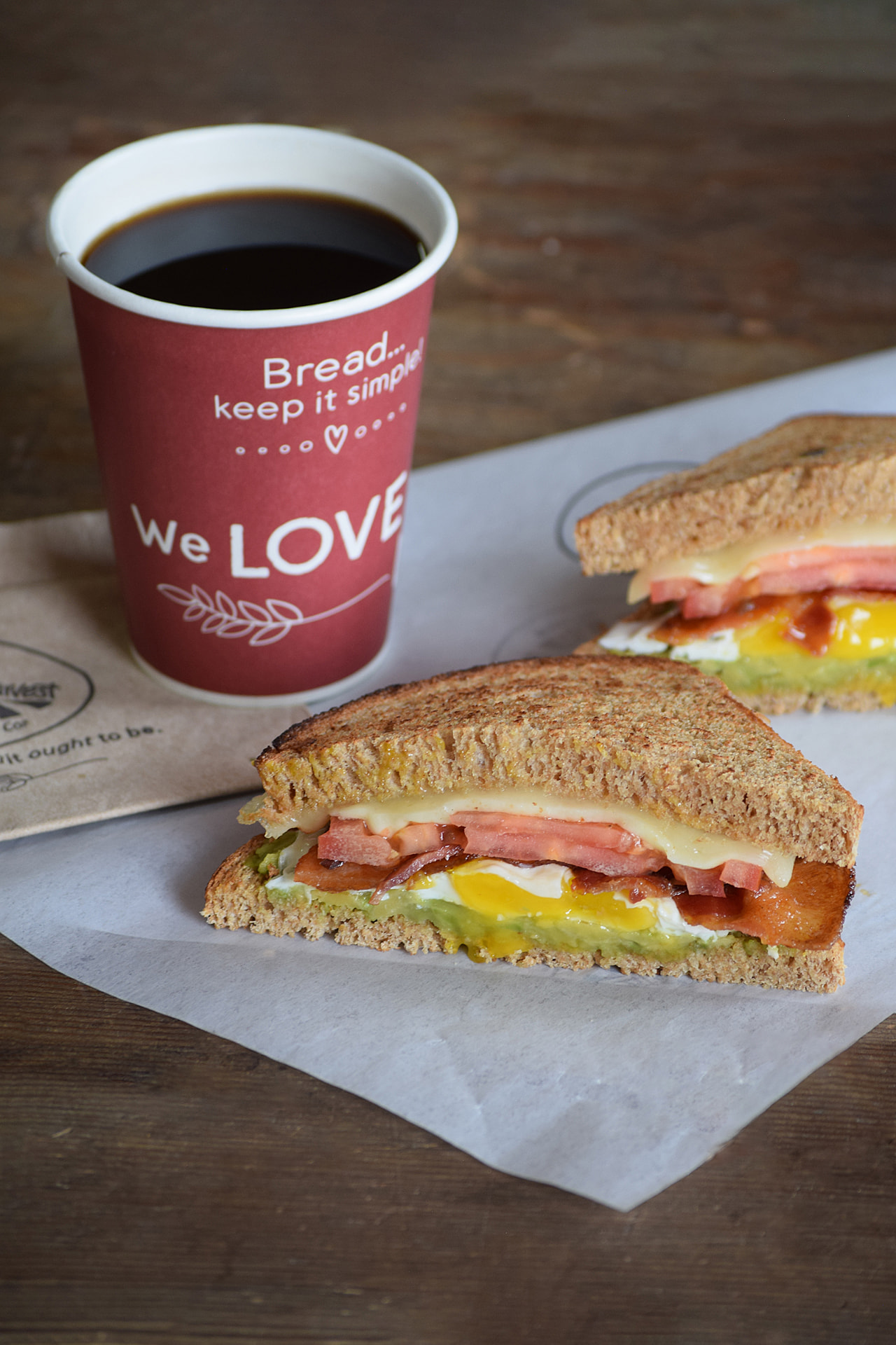 Loaded breakfast sandwich with egg, bacon, avocado, tomato and melted cheese, served with a cup of Great Harvest coffee
