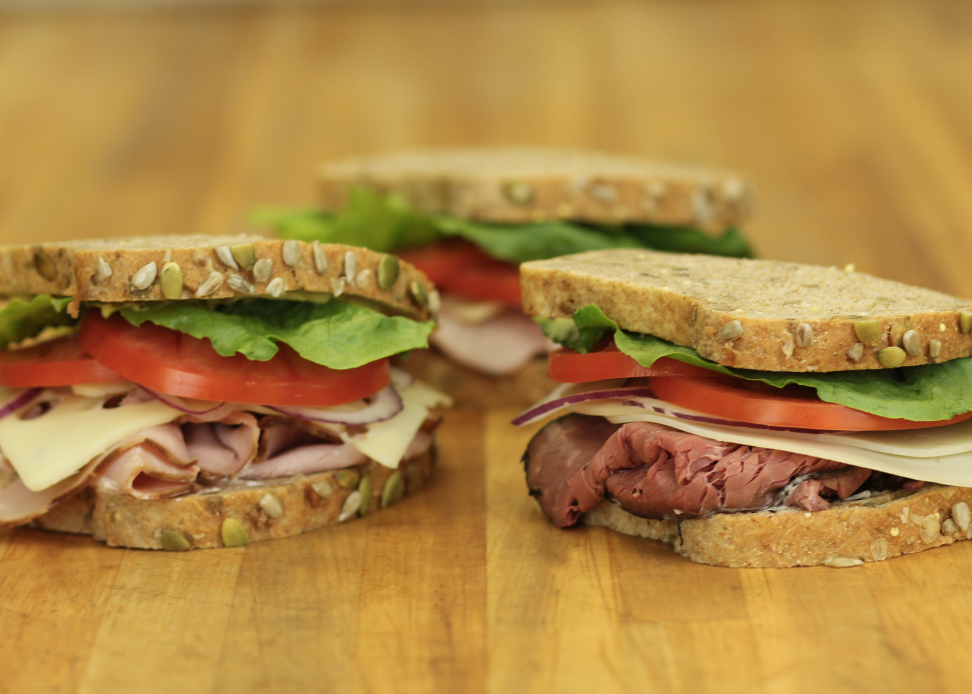 Three handcrafted sandwiches on seeded Great Harvest bread, stacked with fresh meats, cheese, lettuce and tomato